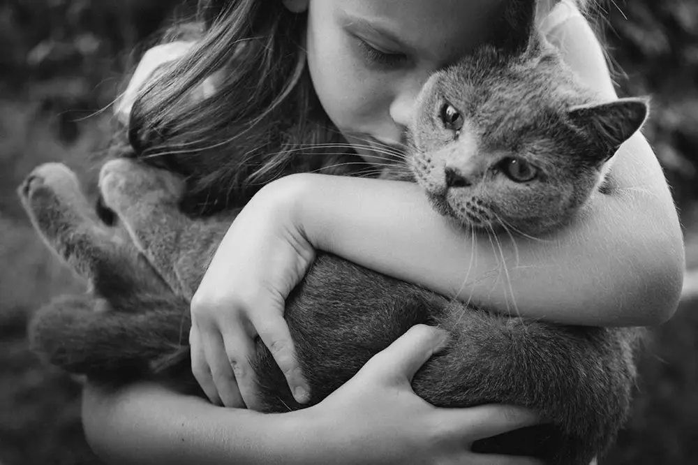 photo noir et blanc enfant tenant un chat dans ses bras et lui faisant un câlin. 