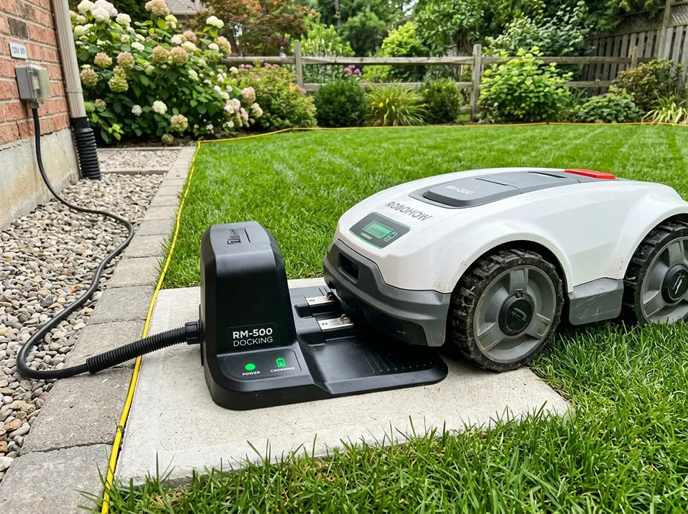 Robot tondeuse se rechargeant sur sa station de charge installée sur sol plat dans un jardin avec indicateurs LED